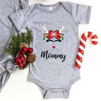 Folded red or white unisex Christmas T-shirt with a simple reindeer graphic design, styled beside ornaments and pine décor for a cozy holiday look.