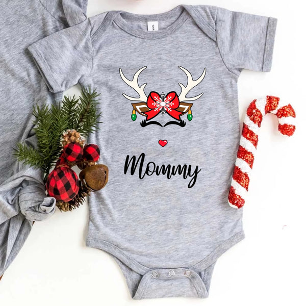 Folded red or white unisex Christmas T-shirt with a simple reindeer graphic design, styled beside ornaments and pine décor for a cozy holiday look.