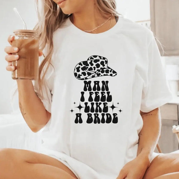 Person wearing a white t-shirt with a cowgirl hat graphic and text, holding a drink.