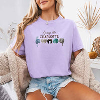 May include a person wearing a Orchid Gossip Like Charlotte Wigs Comfort Colors T-Shirt featuring historical drama inspired graphic and relaxed fit.