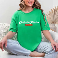 Person wearing a green t-shirt with 'Celebrating Freedom' text, sitting on a couch.