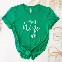 Green maternity t-shirt with 'I miss wine' and baby footprints graphic, flat lay.