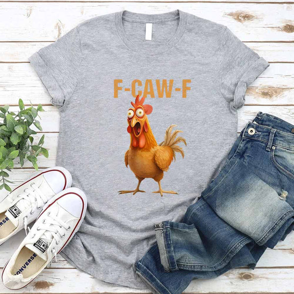 Gray t-shirt with a cartoon rooster and 'F-CAW-F' text, paired with jeans and sneakers on a wooden surface.