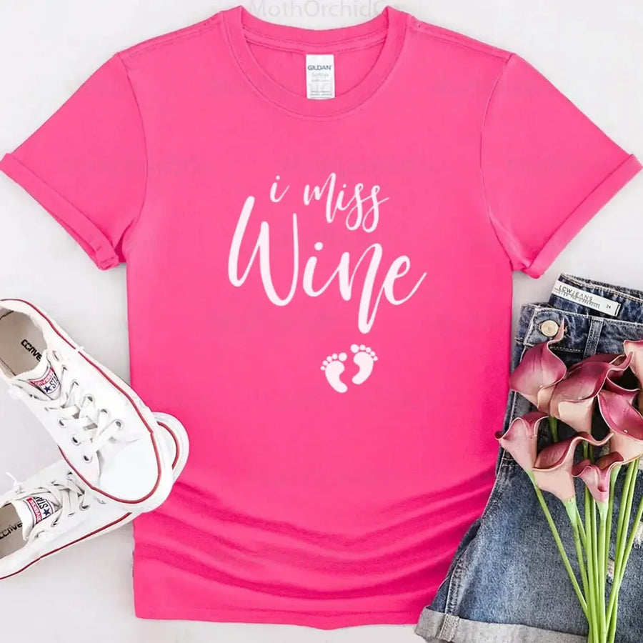Pink custom tee with 'I Miss Wine' text and baby feet graphic, styled with denim shorts, white sneakers, and calla lilies.