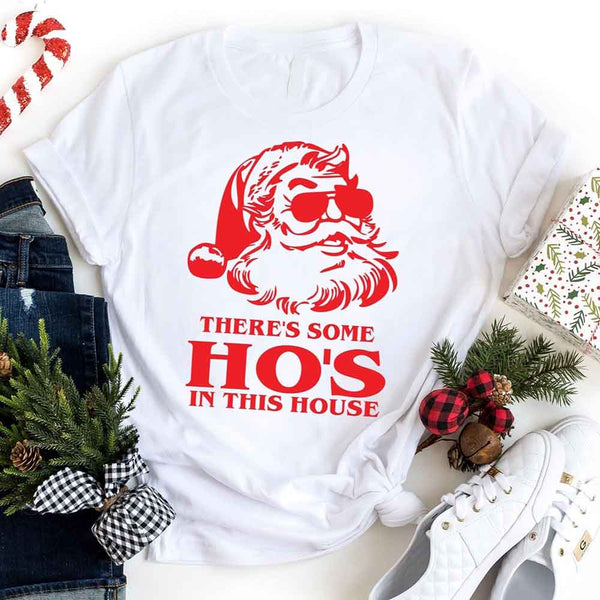 White t-shirt with red Santa Claus graphic and text, surrounded by Christmas decor.