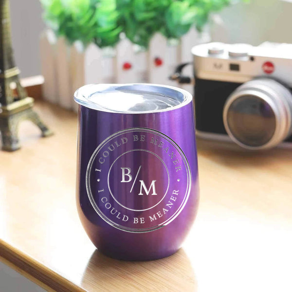 May include a wine tumbler displayed on a wooden surface, featuring a circular black design with the text “I COULD BE MEANER” repeated around the outer ring and the initials “B/M” centered inside. 