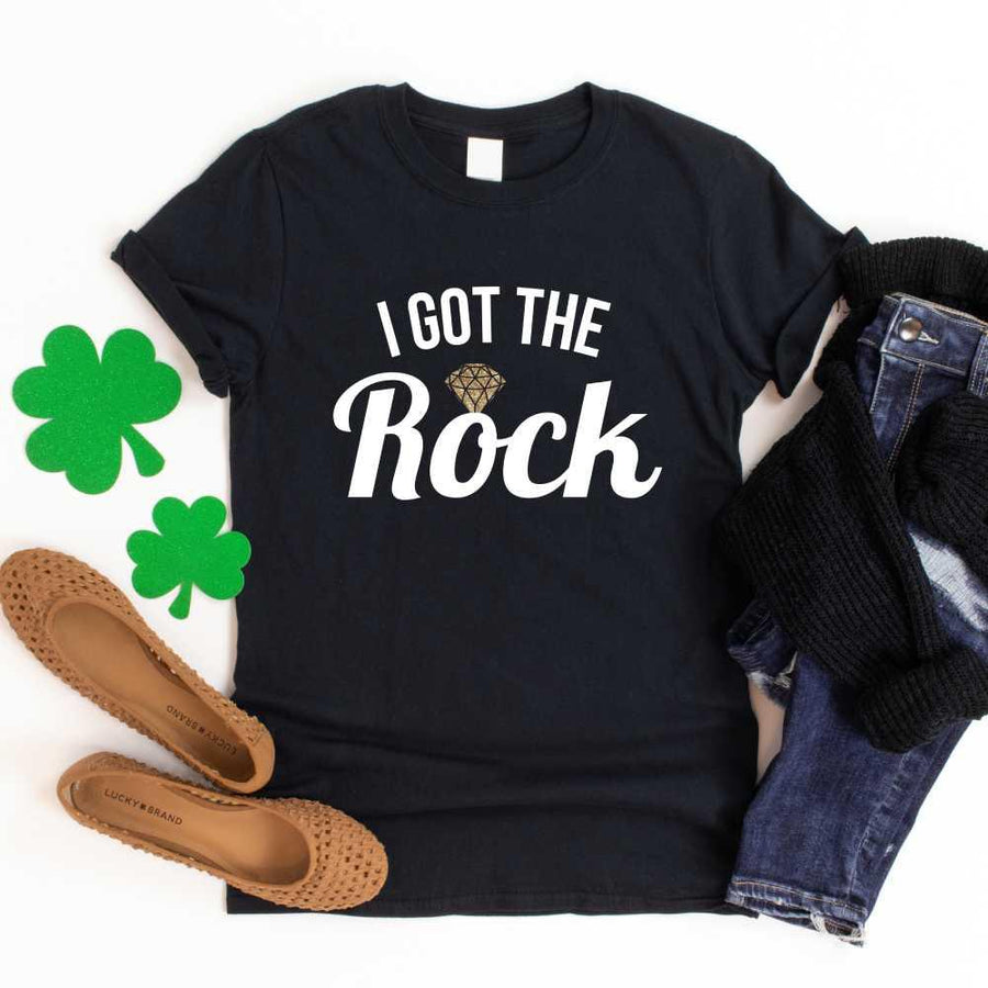 May include a couple wearing matching St. Patrick’s Day engagement t-shirts with the phrase “I Got The Rock”.