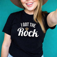 May include a couple wearing matching St. Patrick’s Day engagement t-shirts with the phrase “I Got The Rock”.