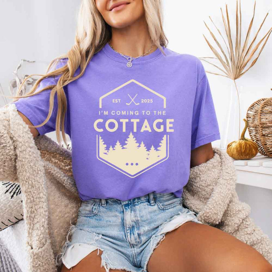 May include a person wearing a Violet I’m Coming to the Cottage T-Shirt featuring rivalry inspired graphic design and relaxed fit.