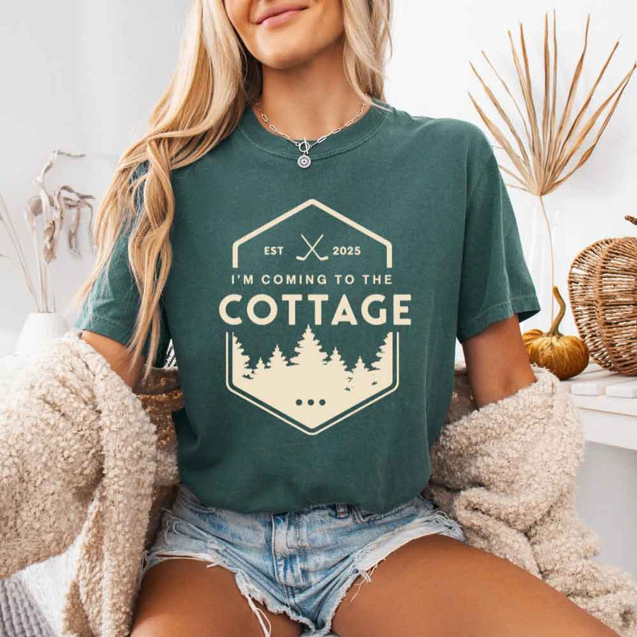 May include a person wearing a Blue Spruce I’m Coming to the Cottage T-Shirt featuring rivalry inspired graphic design and relaxed fit.