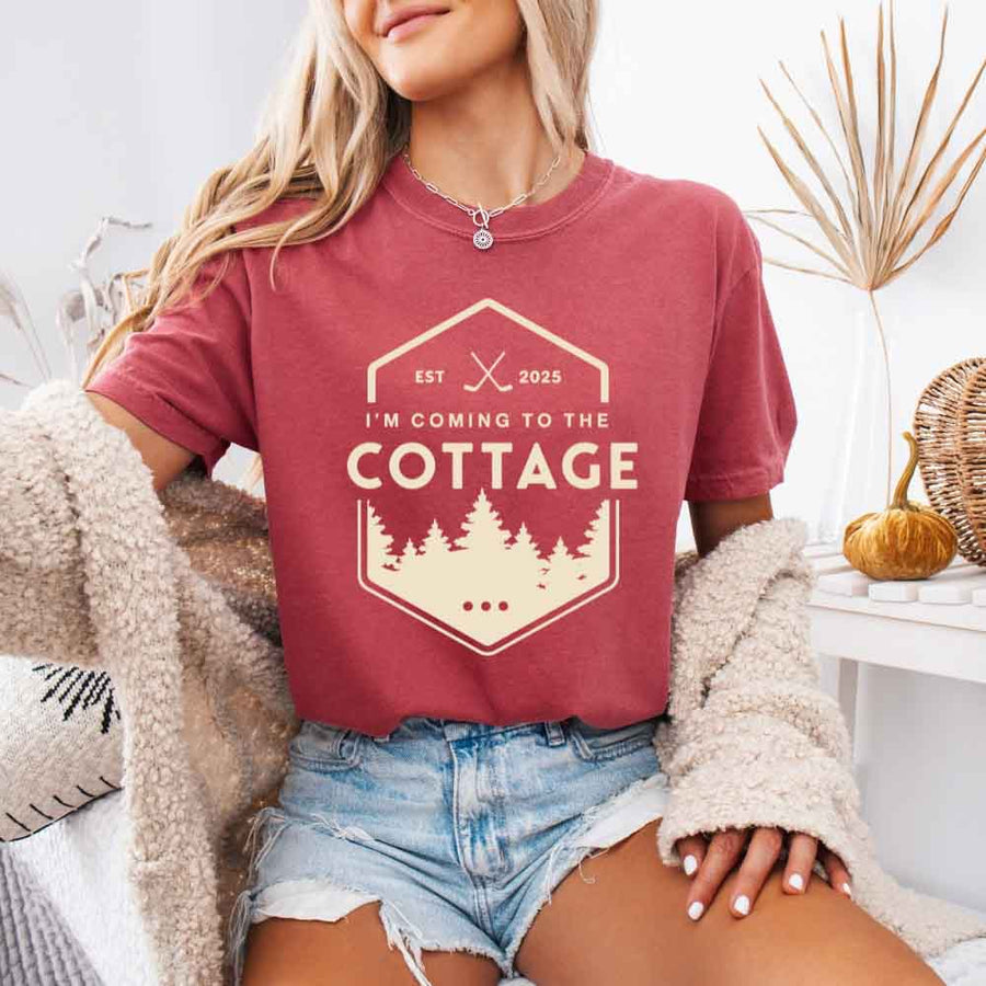 May include a person wearing a Crimson I’m Coming to the Cottage T-Shirt featuring rivalry inspired graphic design and relaxed fit.
