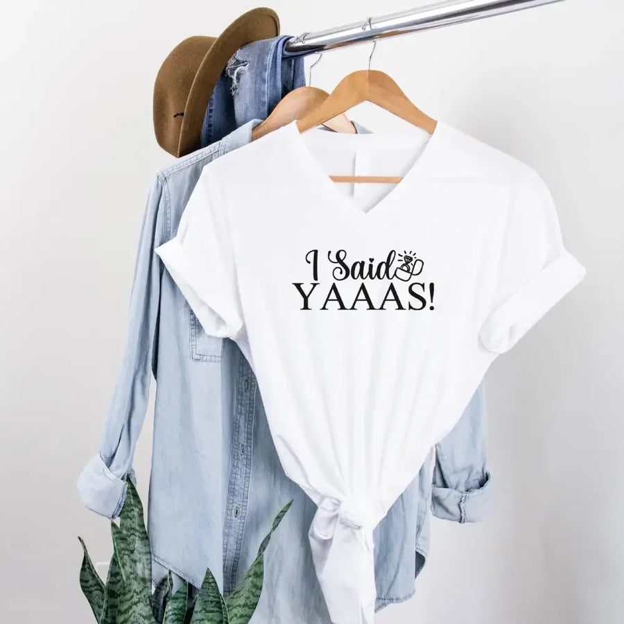 White t-shirt with 'I Said YAAAS!' text on a hanger with denim jacket and hat.