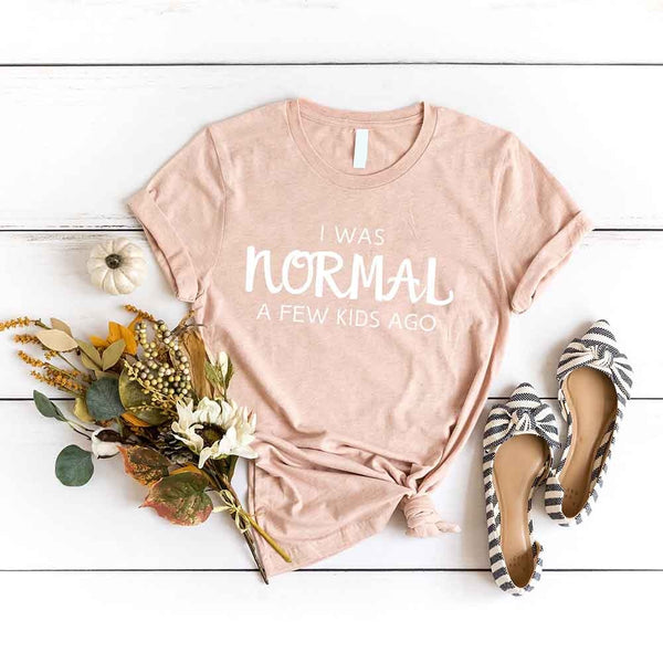 May include a women’s t-shirt with the phrase “I Was Normal a Few Kids Ago,” displayed flat or worn by a mom, highlighting a humorous motherhood theme.