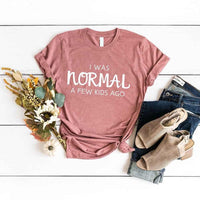 May include a women’s t-shirt with the phrase “I Was Normal a Few Kids Ago,” displayed flat or worn by a mom, highlighting a humorous motherhood theme.