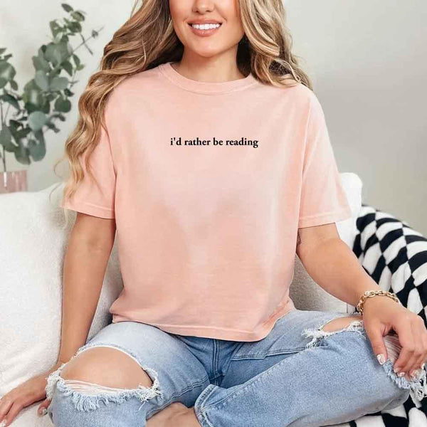 May include a person wearing a peach I'd Rather Be Reading T-Shirt featuring trendy book lover graphic and relaxed fit.
