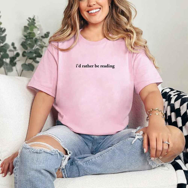 May include a person wearing a pink I'd Rather Be Reading T-Shirt featuring trendy book lover graphic and relaxed fit.
