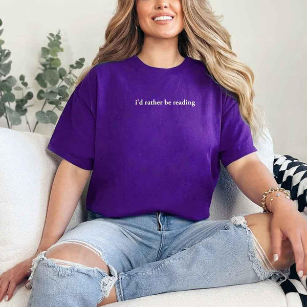 May include a person wearing a purple I'd Rather Be Reading T-Shirt featuring trendy book lover graphic and relaxed fit.
