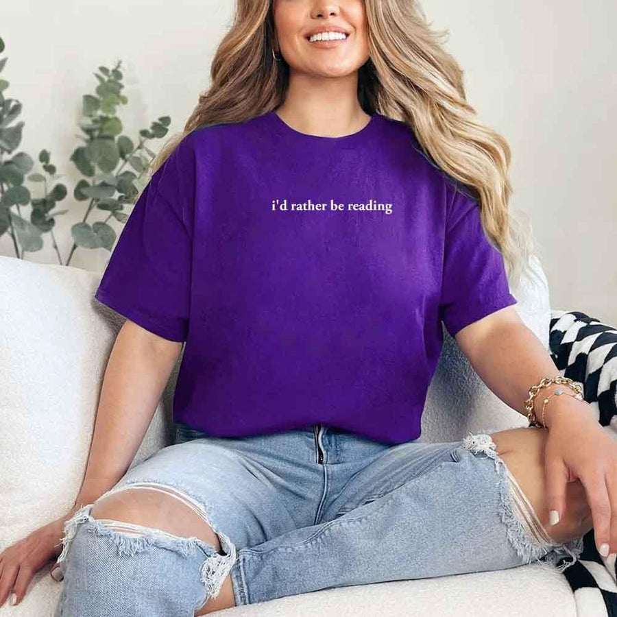 May include a person wearing a purple I'd Rather Be Reading T-Shirt featuring trendy book lover graphic and relaxed fit.
