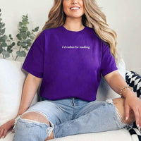 May include a person wearing a purple I'd Rather Be Reading T-Shirt featuring trendy book lover graphic and relaxed fit.
