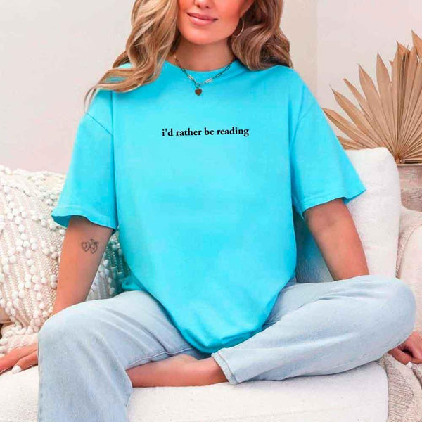 May include a person wearing a turquoise I'd Rather Be Reading T-Shirt featuring trendy book lover graphic and relaxed fit.
