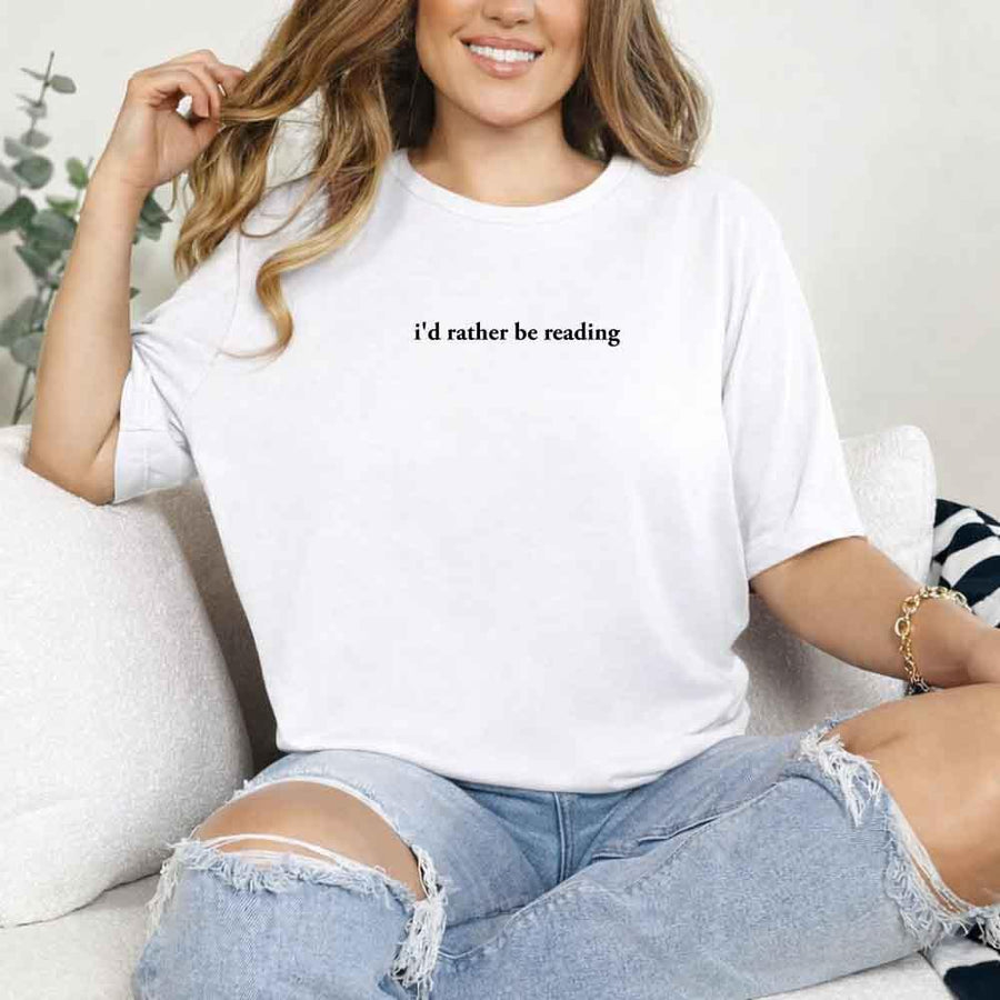 May include a person wearing a white I'd Rather Be Reading T-Shirt featuring trendy book lover graphic and relaxed fit.
