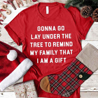 Red t-shirt with humorous text Lay Under A Tree Christmas, Santa hat, and Christmas stocking on a wooden surface.
