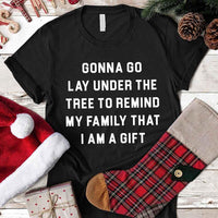 Black t-shirt with Christmas-themed Lay Under A Tree Christmas text on a wooden surface with holiday decorations.