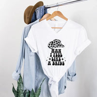 White t-shirt with graphic design and text on a hanger with denim jacket and hat.