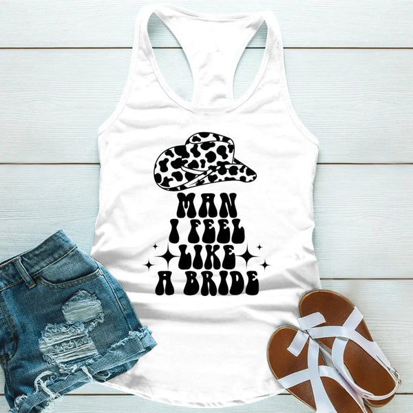White tank top with leopard print hat and text 'Man I Feel Like a Bride' on a light wooden surface, accompanied by denim shorts and sandals.