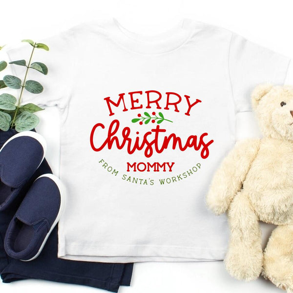May include a festive red and white t-shirt featuring the text “Merry Christmas” and a personalized family name design, laid flat with holiday decorations.