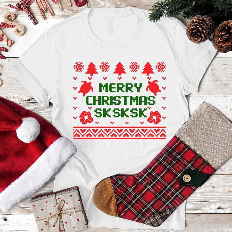 White t-shirt with Christmas-themed design featuring a red and green sweater pattern, surrounded by festive items on a wooden surface.