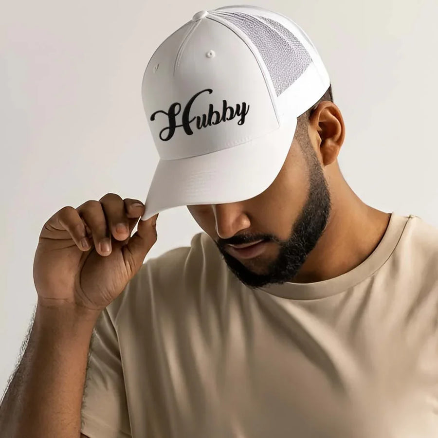 May include an embroidered trucker hat featuring the word “Hubby” stitched in clean, classic lettering on the front panel, designed with a structured crown and breathable mesh back for a timeless wedding or anniversary accessory.