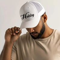 May include an embroidered trucker hat featuring the word “Hubby” stitched in clean, classic lettering on the front panel, designed with a structured crown and breathable mesh back for a timeless wedding or anniversary accessory.