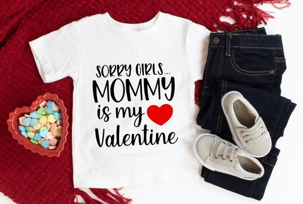 White t-shirt with 'Sorry girls... Mommy is my Valentine' text, paired with jeans and sneakers on a red textured surface.