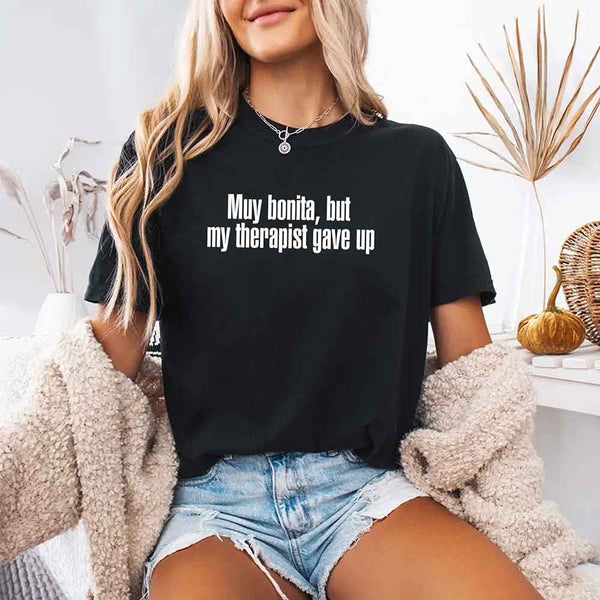 May include a person wearing a black colored sarcastic graphic t-shirt with the phrase “Muy Bonita But My Therapist Gave Up”.
