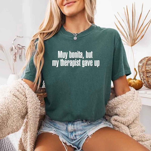 May include a person wearing a blue spruce colored sarcastic graphic t-shirt with the phrase “Muy Bonita But My Therapist Gave Up”.
