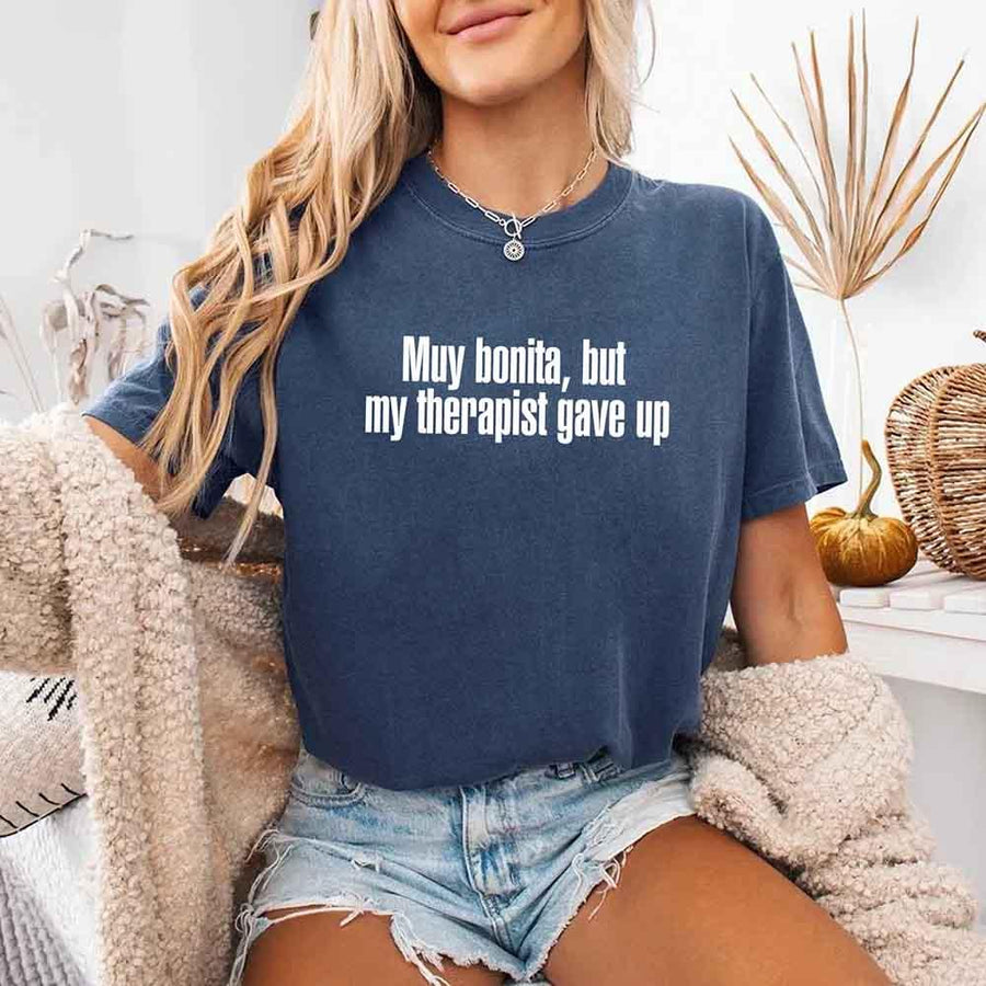 May include a person wearing a denim colored sarcastic graphic t-shirt with the phrase “Muy Bonita But My Therapist Gave Up”.

