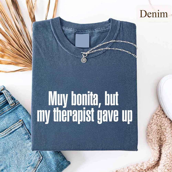 May include a person wearing a denim colored sarcastic graphic t-shirt with the phrase “Muy Bonita But My Therapist Gave Up”.
