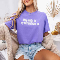 May include a person wearing a violet colored sarcastic graphic t-shirt with the phrase “Muy Bonita But My Therapist Gave Up”.
