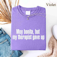 May include a person wearing a violet colored sarcastic graphic t-shirt with the phrase “Muy Bonita But My Therapist Gave Up”.
