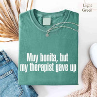 May include a person wearing a light green colored sarcastic graphic t-shirt with the phrase “Muy Bonita But My Therapist Gave Up”.

