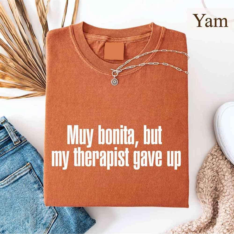 May include a person wearing a yam colored sarcastic graphic t-shirt with the phrase “Muy Bonita But My Therapist Gave Up”.
