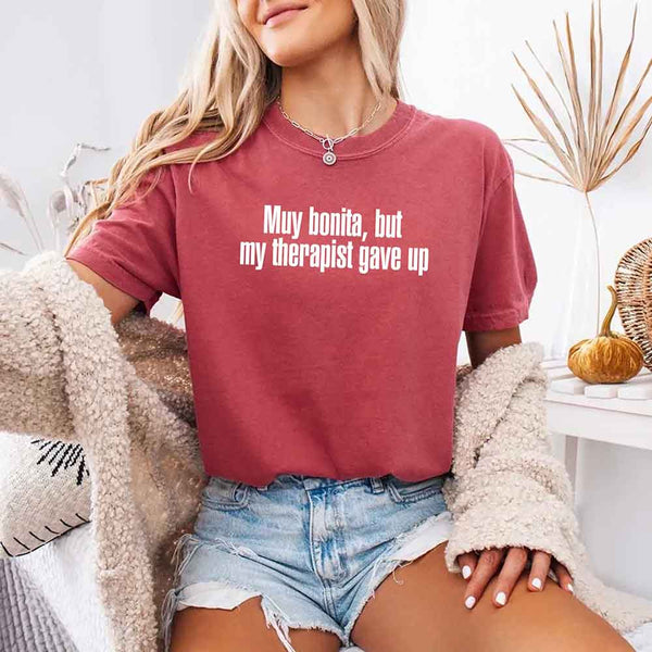 May include a person wearing a crimson colored sarcastic graphic t-shirt with the phrase “Muy Bonita But My Therapist Gave Up”.
