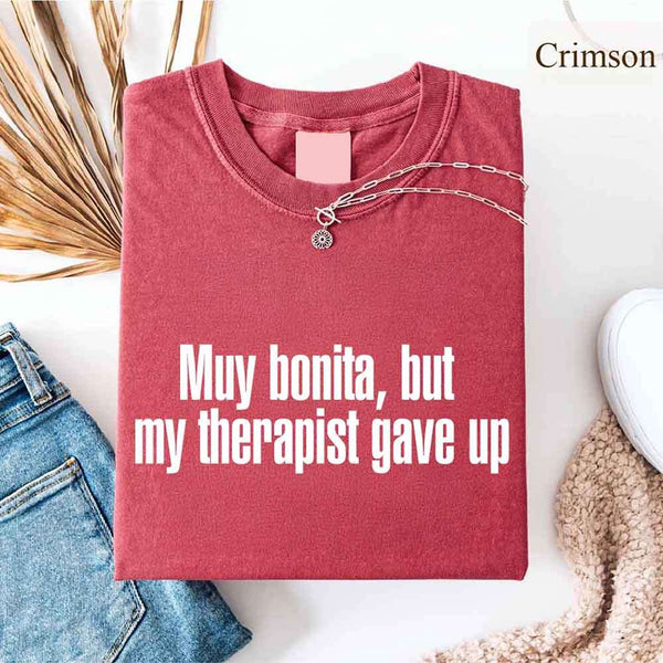 May include a person wearing a crimson colored sarcastic graphic t-shirt with the phrase “Muy Bonita But My Therapist Gave Up”.
