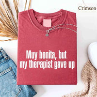May include a person wearing a crimson colored sarcastic graphic t-shirt with the phrase “Muy Bonita But My Therapist Gave Up”.
