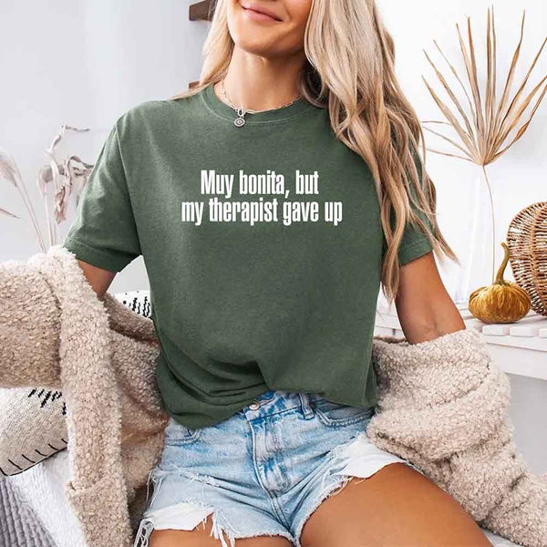 May include a person wearing a moss colored sarcastic graphic t-shirt with the phrase “Muy Bonita But My Therapist Gave Up”.
