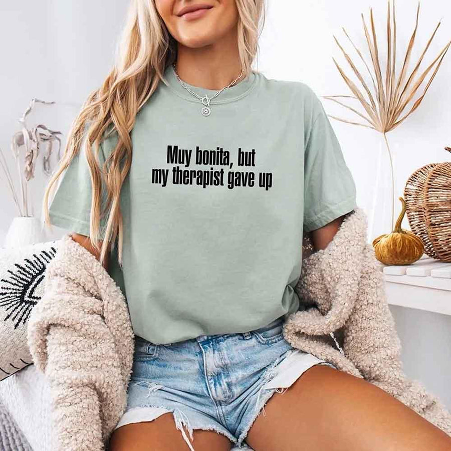 May include a person wearing a bay colored sarcastic graphic t-shirt with the phrase “Muy Bonita But My Therapist Gave Up”.

