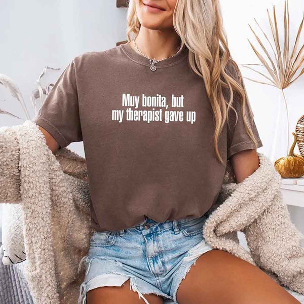 May include a person wearing an expresso colored sarcastic graphic t-shirt with the phrase “Muy Bonita But My Therapist Gave Up”.
