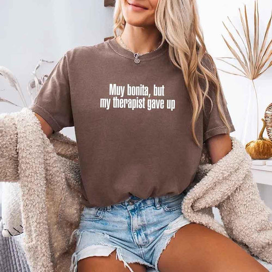 May include a person wearing an expresso colored sarcastic graphic t-shirt with the phrase “Muy Bonita But My Therapist Gave Up”.
