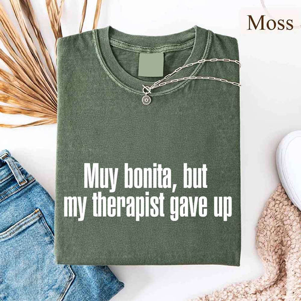 May include a person wearing a moss colored sarcastic graphic t-shirt with the phrase “Muy Bonita But My Therapist Gave Up”.
